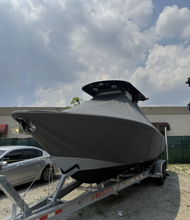Custom Sunbrella charcoal gray full boat cover on a 32 Sportsman center console on a trailer, covering the hull sides and tapering over the transom